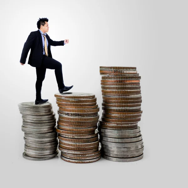 Biznesmen, chodzenie na stos monet na szarym tle — Zdjęcie stockowe