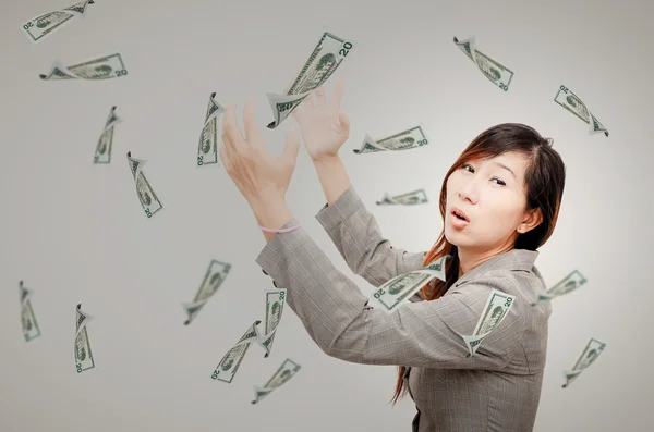 Glada affärskvinna försöker fånga pengar regn på grå bakgrunds — Stockfoto