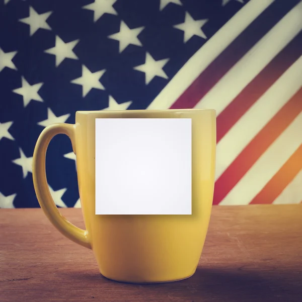 Taza de café amarillo sobre mesa de madera con fondo de bandera de EE.UU. — Foto de Stock