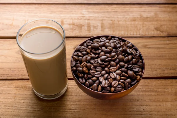 Chicchi di caffè in ciotola e un bicchiere di latte di caffè sul tavolo di legno . — Foto Stock