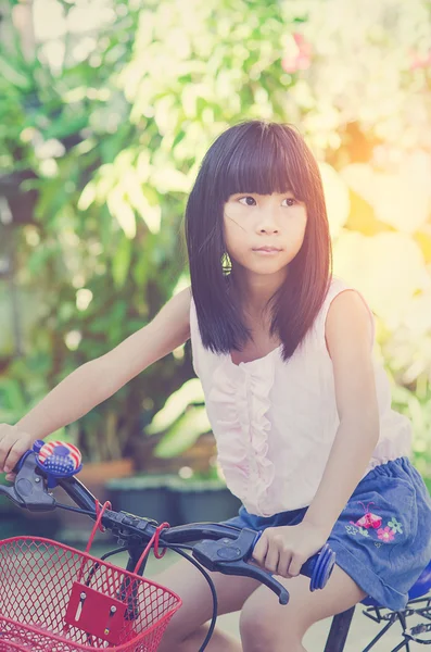 De cerca chica asiática montando su triciclo en el soleado parque de verano. Ki. — Foto de Stock