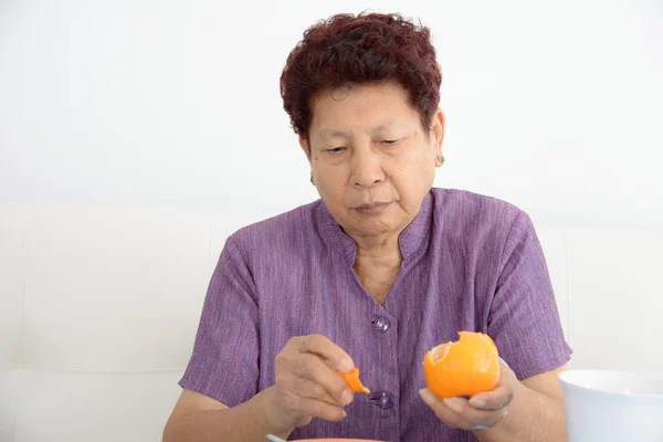 Ernstige Aziatische senior vrouw oranje thuis eten. — Stockfoto