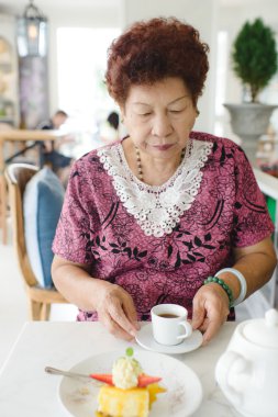 Cafe 'de çay içen mutlu Asyalı son sınıf öğrencisi kadın.