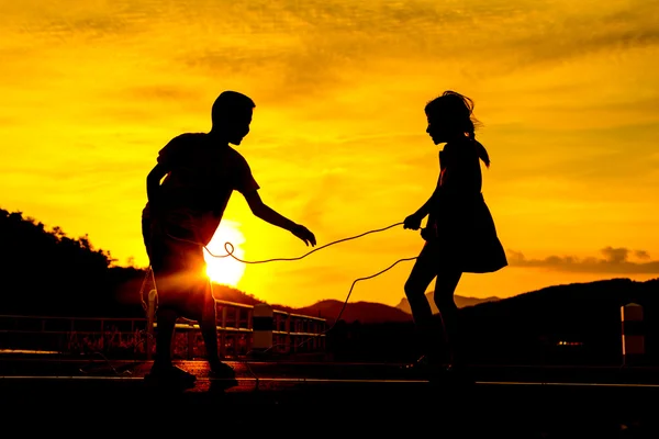 Siluetă, copii fericiţi jucând Tug of war pe pajişte, apus de soare , — Fotografie, imagine de stoc