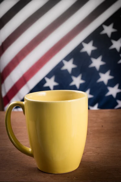 Taza de café amarillo sobre mesa de madera con fondo de bandera de EE.UU. . — Foto de Stock