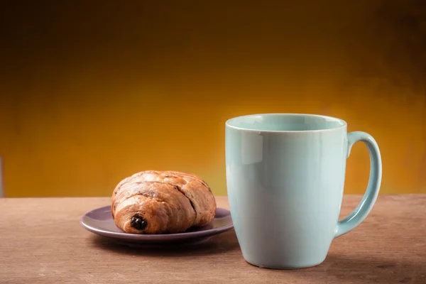 Blaue Kaffeetasse mit Croissant auf Holztisch. — Stockfoto