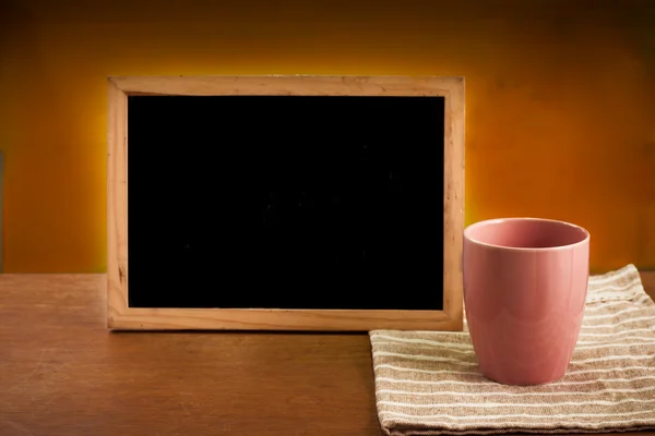 Pembe çay bardağı ve ahşap masa kara tahta — Stok fotoğraf