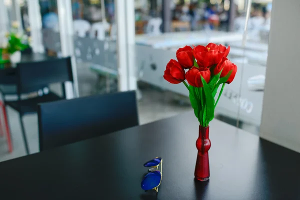 Ваза с тюльпаном и синие солнцезащитные очки на черном столе . — стоковое фото