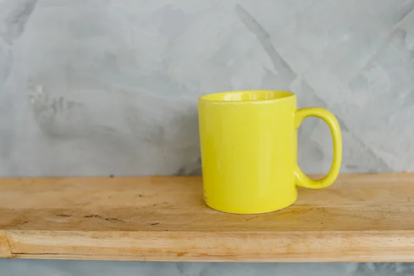 Yellow coffee cup on wooden shelf against grey background. — Stock Photo, Image