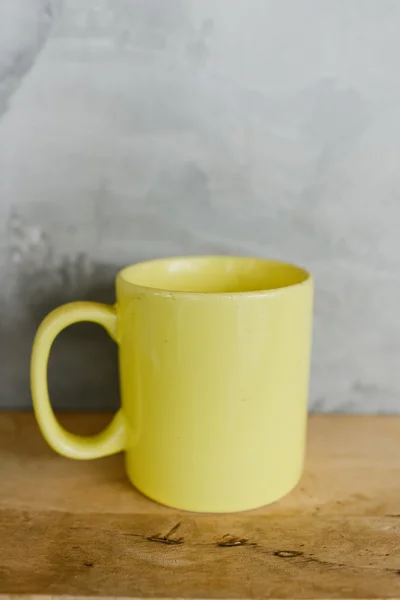 Yellow coffee cup on wooden shelf against grey background. — Stock Photo, Image