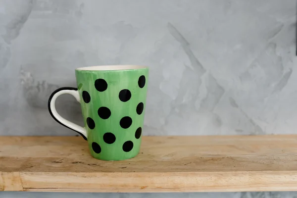 Green cup with dot on wooden background and cement wall. — Stock Photo, Image