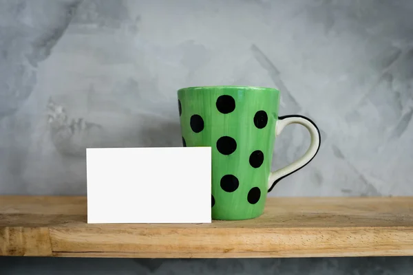 Taza verde con puntos y tarjeta en blanco en estante de madera . — Foto de Stock