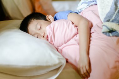 Yatakta uyuyan Asyalı çocuk.