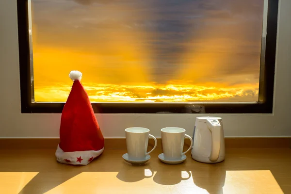 Kerstmuts met een koffiemok in de buurt van venster kijkend naar zonstijging met nb — Stockfoto