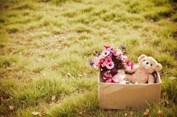 Orso e mazzo di fiori in scatola marrone su erba verde con naturale — Foto Stock