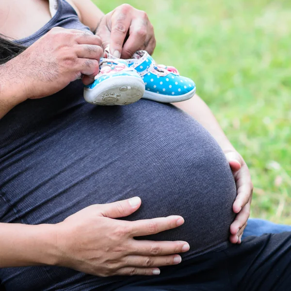 Новорожденные детские сапоги в руках родителей, беременная женщина в животе . — стоковое фото