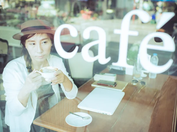 Mujer asiática bebiendo café y usando la computadora en la cafetería . — Foto de Stock