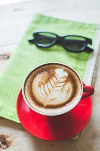 Röd kaffekopp latte art och glasögon på trä bakgrund. — Stockfoto