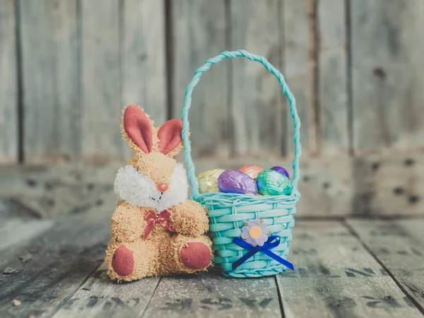 Huevos de Pascua de chocolate en una cesta y muñeca de conejo en la espalda de madera —  Fotos de Stock