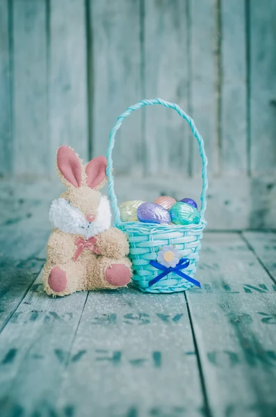 Huevos de Pascua de chocolate en una cesta y muñeca de conejo en la espalda de madera —  Fotos de Stock