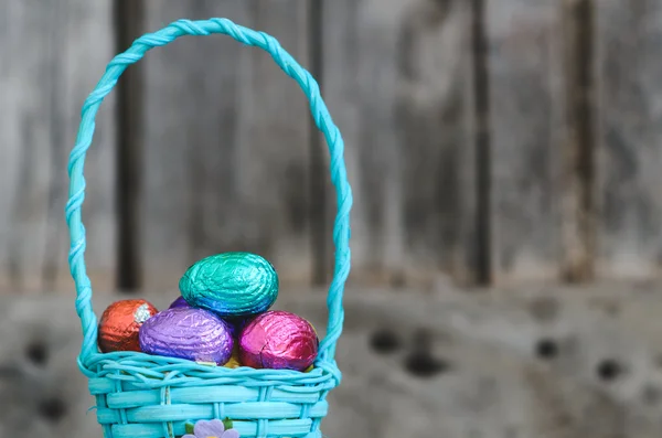 Huevos de Pascua de chocolate coloridos en canasta azul sobre fondo de madera — Foto de Stock