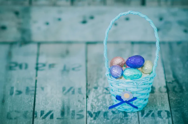 Huevos de Pascua de chocolate coloridos en canasta azul sobre fondo de madera — Foto de Stock