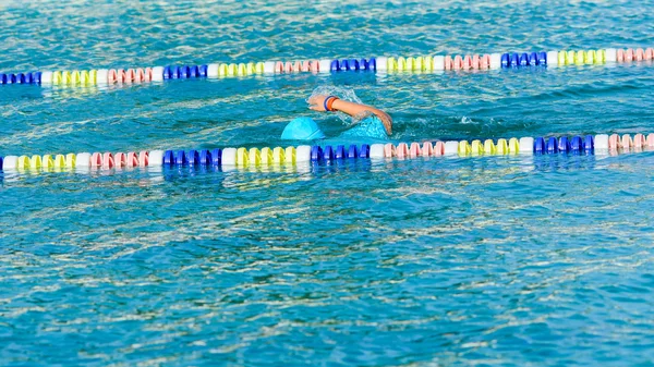 Schwimmerin schwimmt im blauen Wasser und trägt eine blaue Mütze — Stockfoto