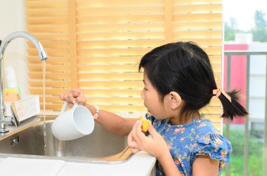 Asyalı kız mutfakta beyaz Kupası yıkama.