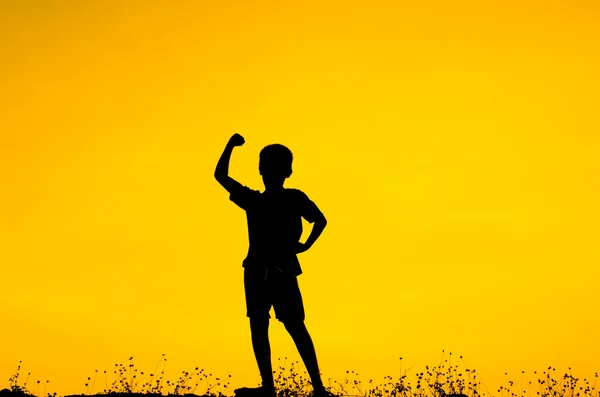 Menino levantando as mãos de pé durante o pôr do sol — Fotografia de Stock