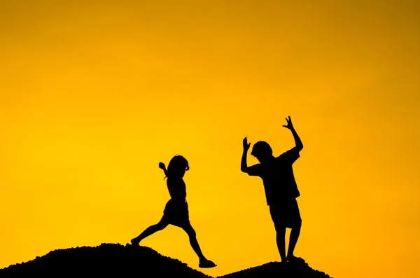 Мальчик и девочка поднимают руки, стоя на вершине холма под солнцем — стоковое фото