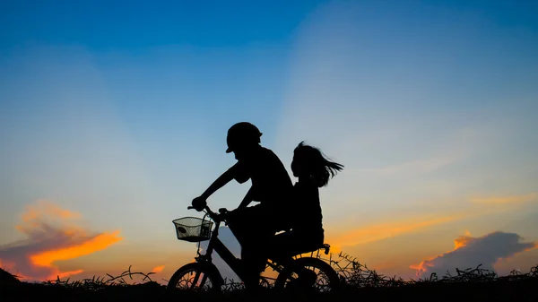 他的姐姐在夕阳的背景上骑自行车的男孩。Silhouet — 图库照片