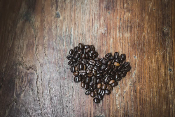 Heart shape made from coffee beans on wooden surface. — Stock Photo, Image