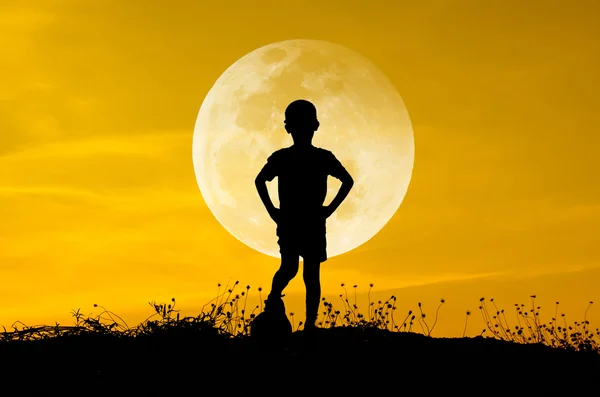 Boy with soccer ball, big moon and grass silhouettes background — Stock Photo, Image