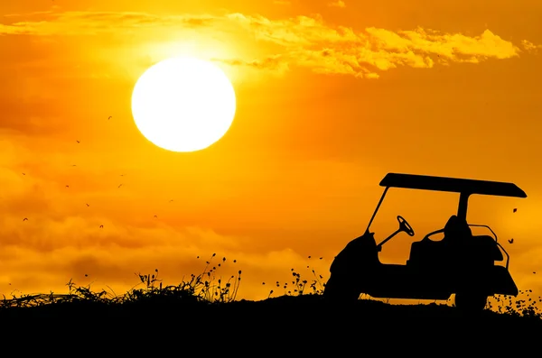 Carrinho de golfe na grama silhuetas fundo com pôr do sol . — Fotografia de Stock