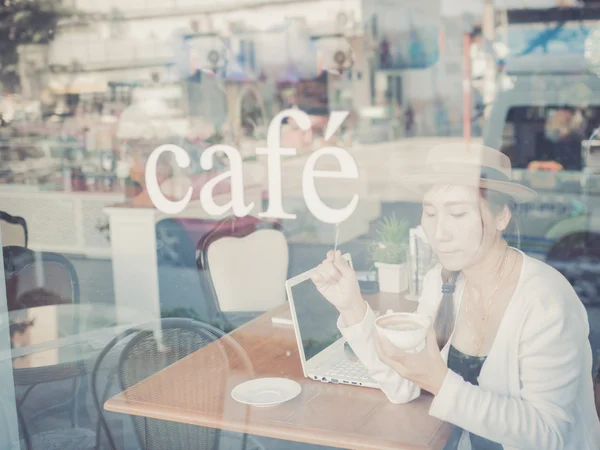 Asiatische Frau, die Kaffee trinkt und Computer im Café benutzt. Foto: — Stockfoto