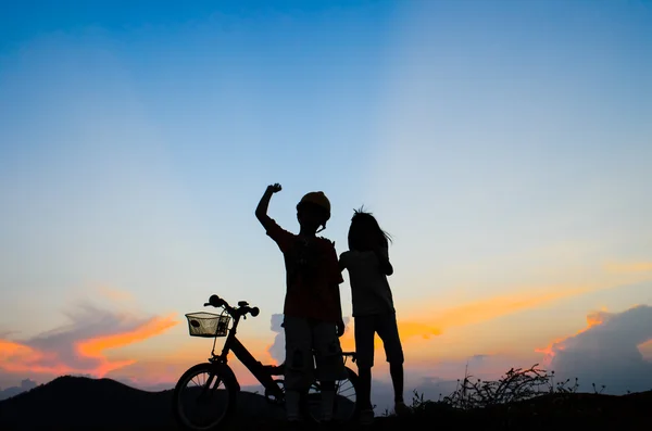 Pojken med sin syster rida cykel på sunset bakgrund. Silhouet — Stockfoto