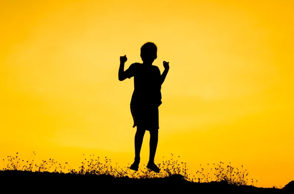 Menino levantando as mãos de pé durante o pôr do sol — Fotografia de Stock