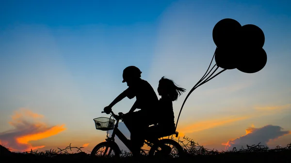 他的姐姐在夕阳的背景上骑自行车的男孩。Silhouet — 图库照片