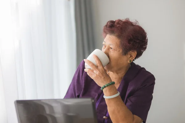 Asijské starší žena učení poznámkového bloku a pít čaj v h — Stock fotografie