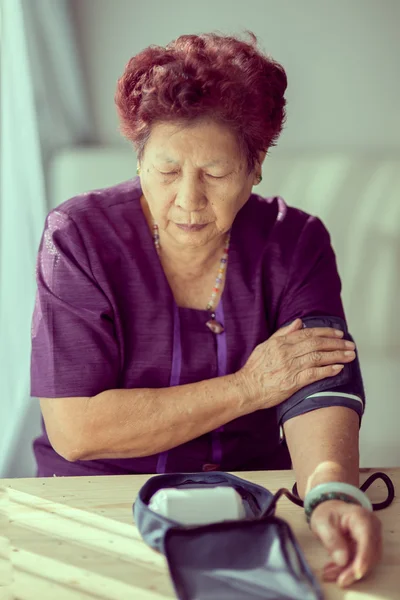Азиатская старшая женщина проверяет кровяное давление с помощью оконного света и — стоковое фото
