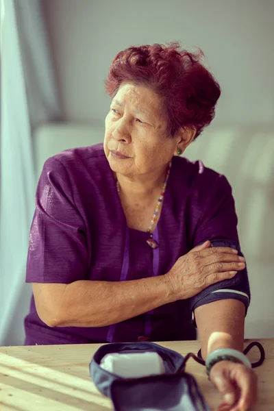 Aziatische senior vrouw controleren bloeddruk met venster licht en — Stockfoto