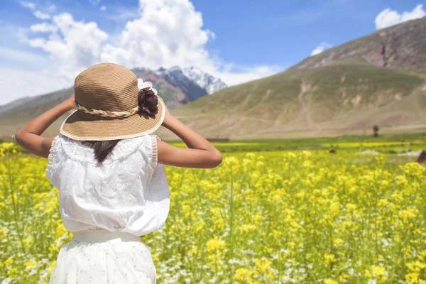 Achterkant meisje met hoed met bloeiende bloem veld achtergrond. — Stockfoto
