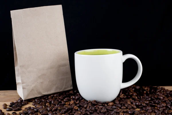 Coffee beans in white cup and brown paper bag on wooden table wi — Stock Photo, Image