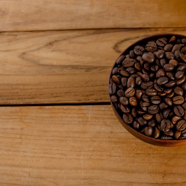 Chicchi di caffè in ciotola su sfondo di legno . — Foto Stock