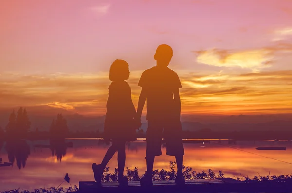 Brother and sister holding hands together with sun set. — Stock Photo, Image