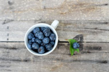 ahşap arka plan üzerinde beyaz fincan taze yaban mersini