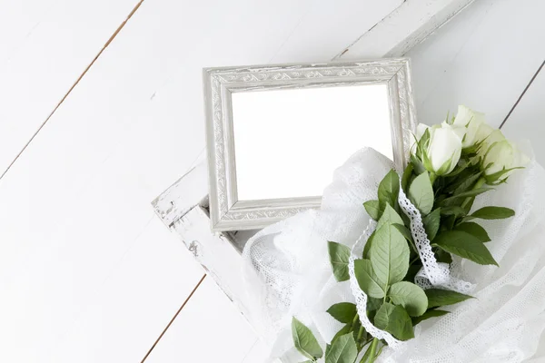 Leerer silberner Bilderrahmen mit fünf weißen Rosen und Spitzenband Stockbild