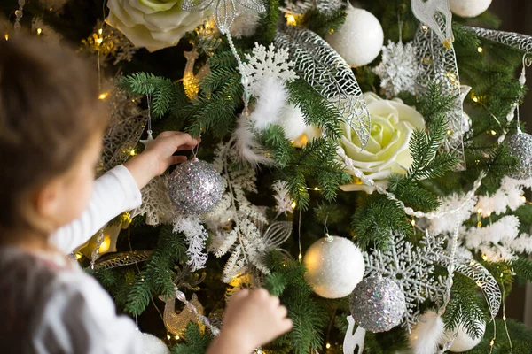小さな女の子が手でクリスマスツリーのおもちゃのために到達します クリスマスの装飾 休日と奇跡を待っています ピンク 青の装飾 ゴールデンライトガーランド — ストック写真