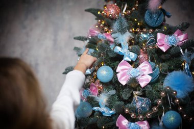 Küçük bir kız eliyle bir Noel ağacı oyuncağına uzanıyor. Noel dekoru, bir tatil ve mucize bekliyor. Yeni yıl. Beyaz, pembe ve mavi dekor, altın renkli çelenkler