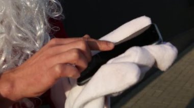 Eldivensiz Noel Baba 'nın eli parmaklarını akıllı telefon ekranında gezdiriyor. Uzun beyaz sakallı, kırmızı elbiseli. Modern Rus büyükbabası Frost. Yeni Yıl Düzenleme İşlemi